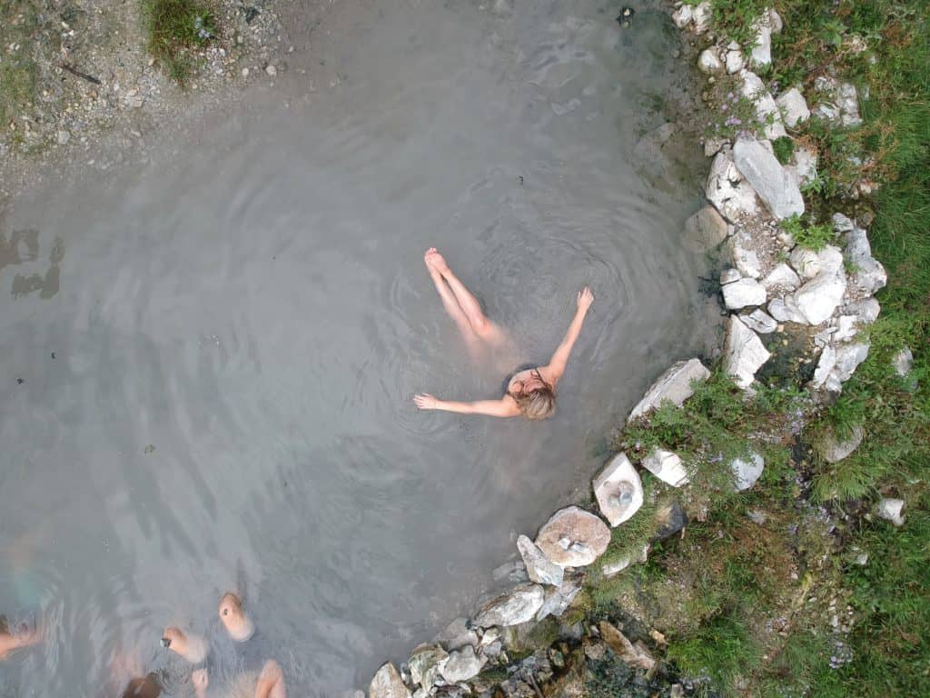 an overhead shot of a woman bathing in a natural hot spring with a rock border