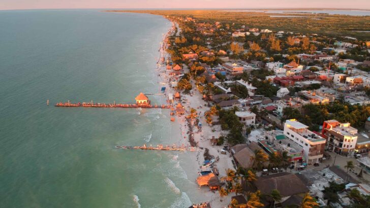 the sun sets over emerald water and an island with white sand