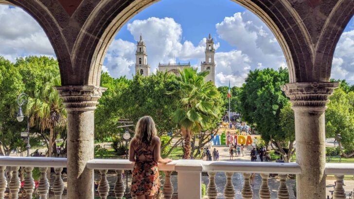 a woman stands under an archway overlooking a plaza with a church