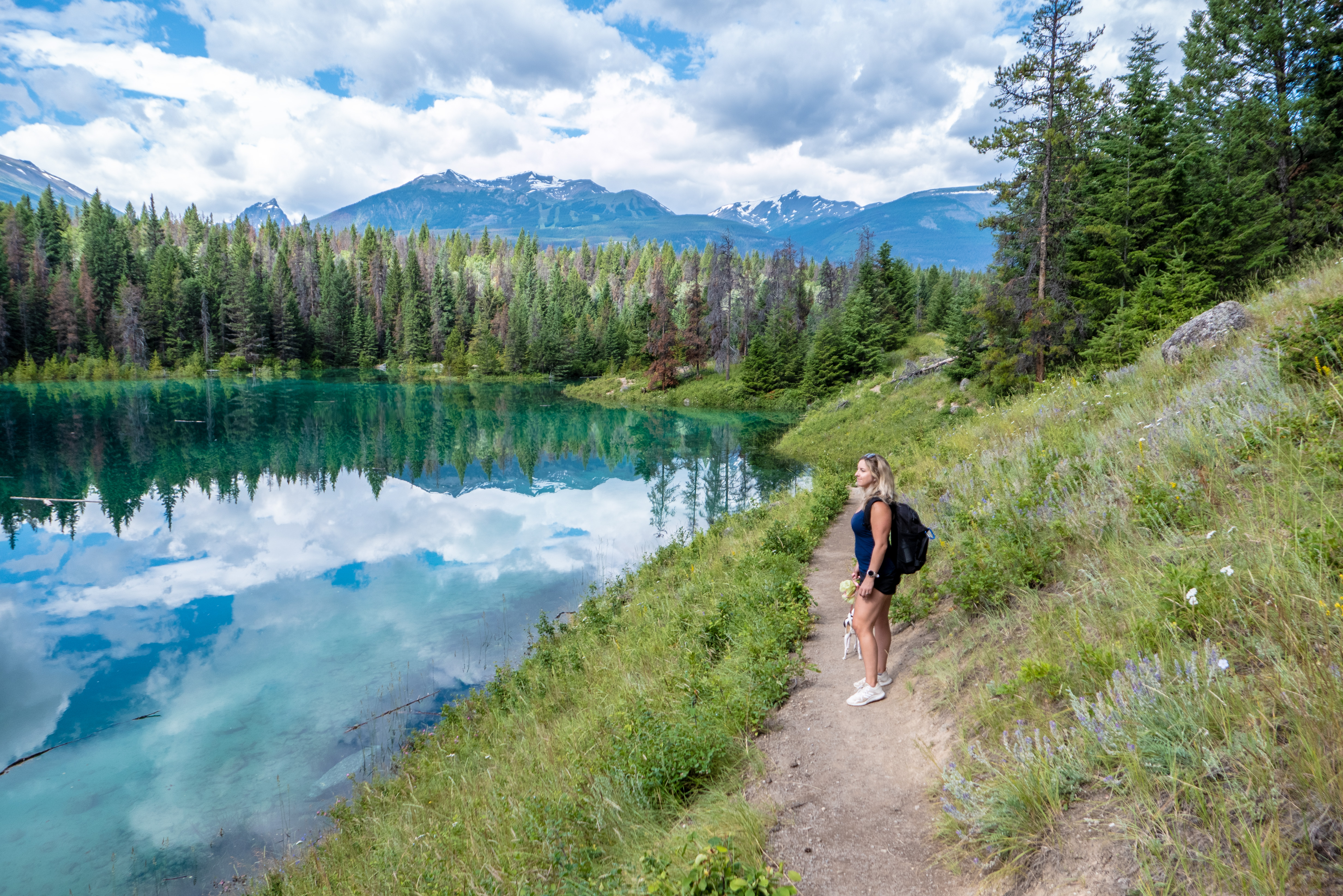 a woman pauses on a trail to look at the turquoise green lake in the alpine forest
