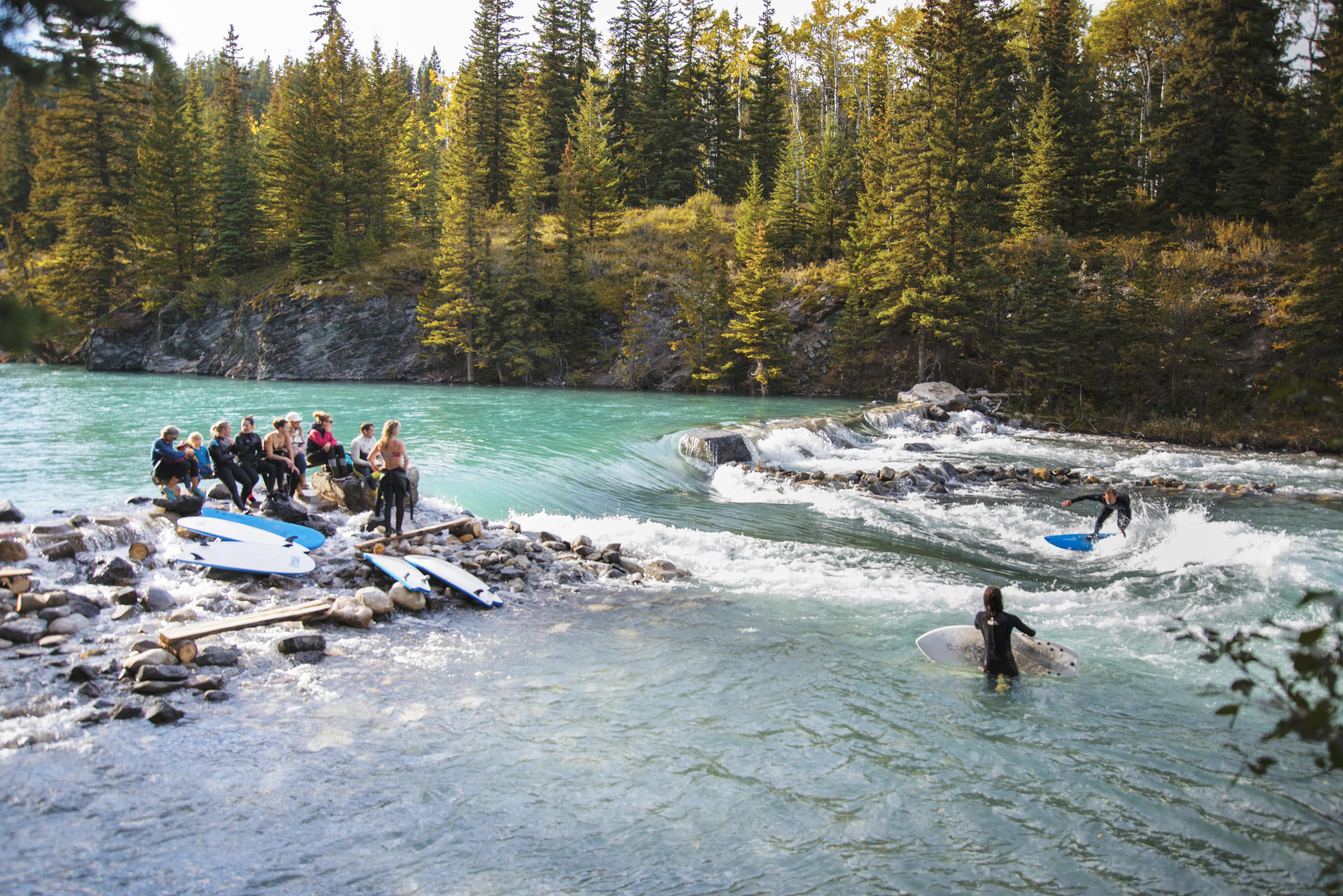 a group of surfers in wetsuits on a river surfing