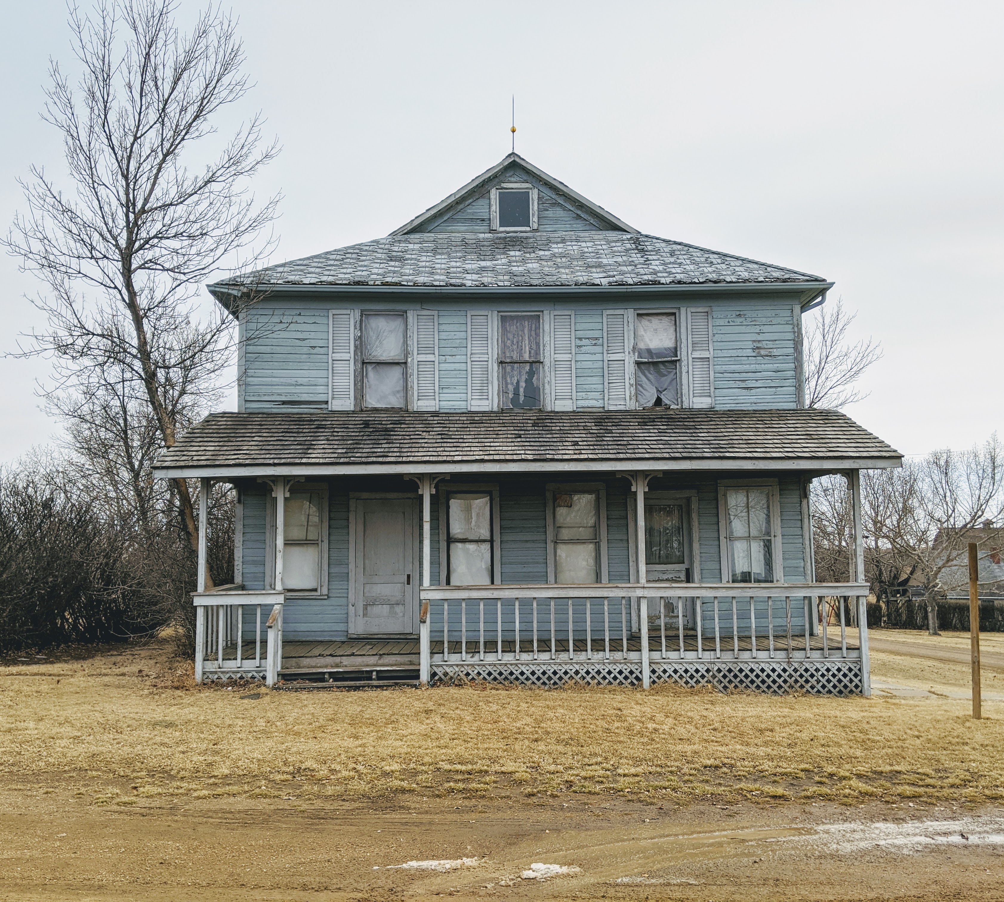an abandoned house with faded and chipped blue paint with a white porch