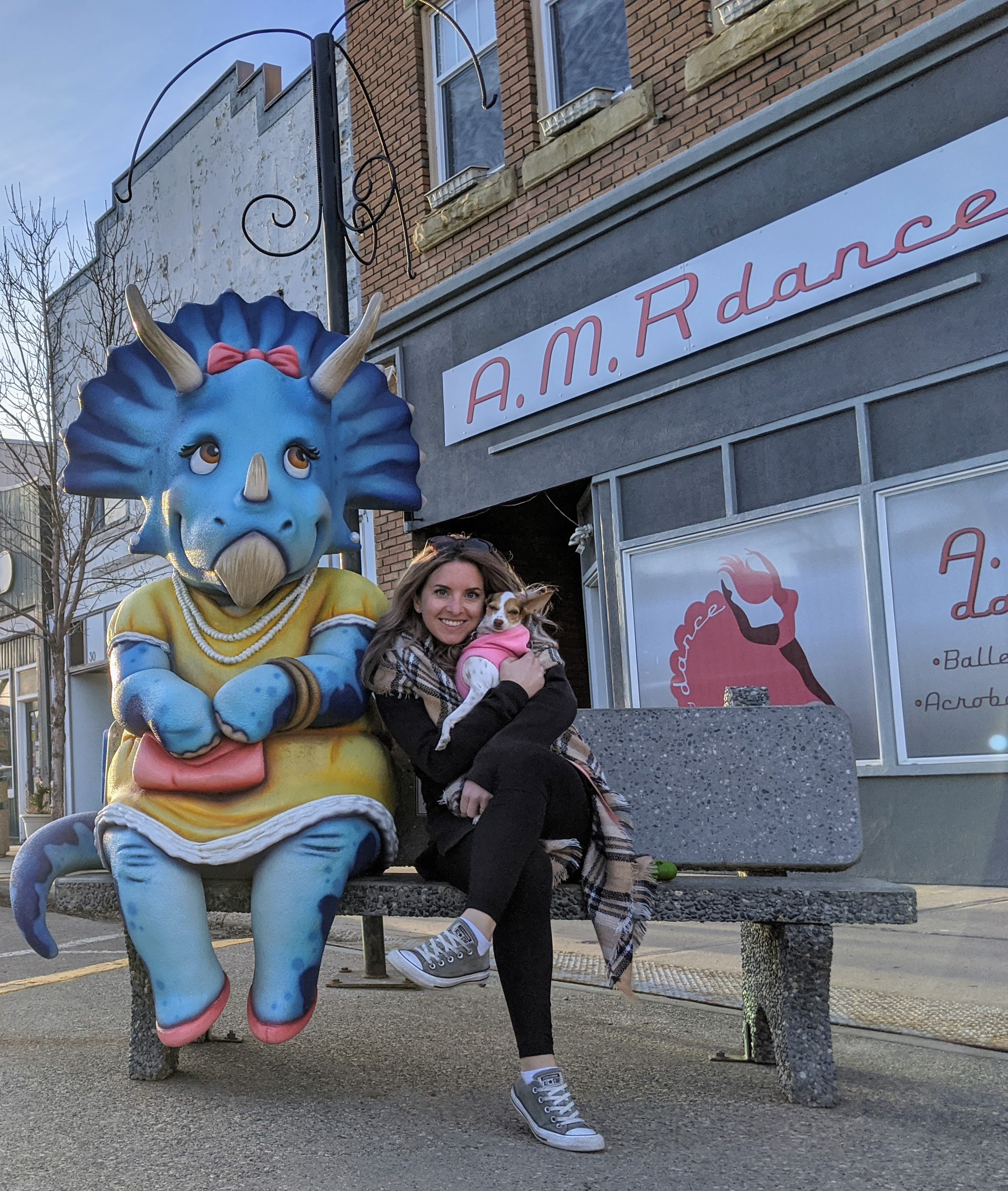 a girl sitting on a bench beside a blue triceratops dinosaur statue