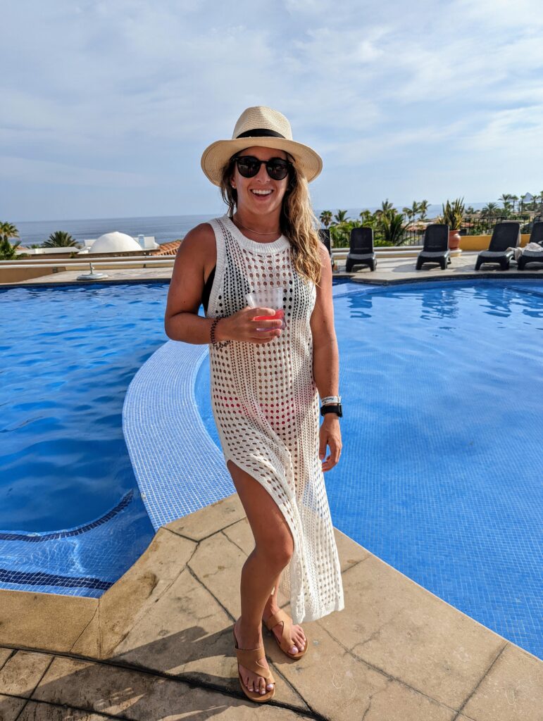 a woman standing in front of a pool wearing a light beige dress